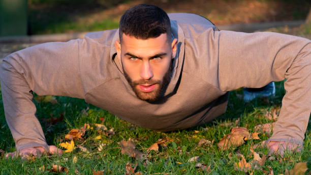 Focused athlete doing push ups on the grass, casual guy doing strength training, beautiful man doing body weight workout stock photo