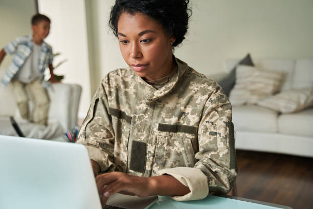 Focused black woman soldier using laptop at table stock photo