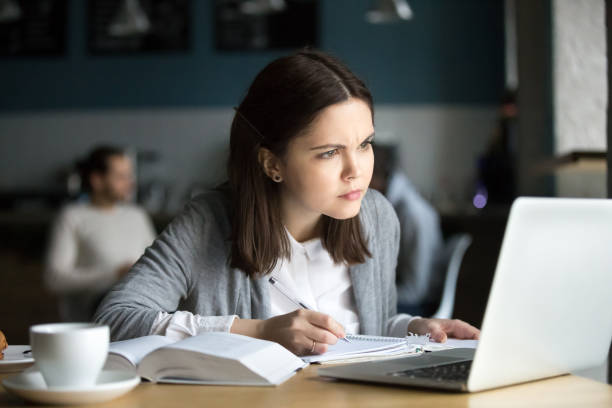 Focused girl concerned about difficult online task studying in cafe Focused girl concerned about difficult online assignment looking at laptop screen studying working in cafe, millennial student thinking of problem solution reading hard task on computer making notes toughest exams stock pictures, royalty-free photos & images