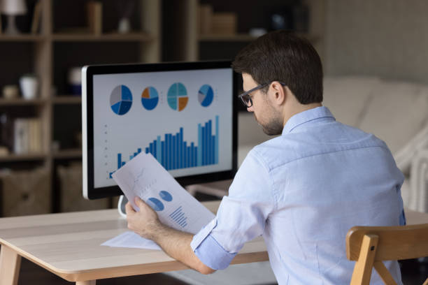Focused millennial business man analyzing marketing reports on desktop monitor stock photo
