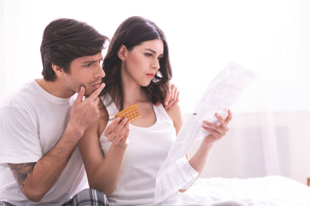 Focused millennial couple reading leaflet before taking contraceptive pills Focused millennial couple reading leaflet before taking contraceptive pills, sitting on bed, empty space contraceptive stock pictures, royalty-free photos & images