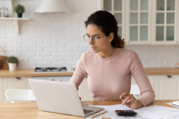 Focused millennial woman in eyeglasses paying bills online. stock photo