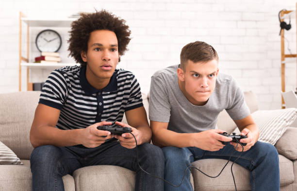 adolescenti concentrati che giocano ai videogiochi insieme sul divano - joystick soccer foto e immagini stock