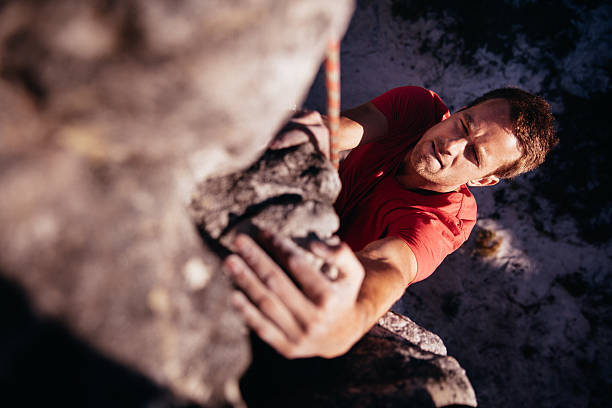 Focussed Rock climber holding on grip while hanging from boulder Rock climber gathering strength to climb higher while he is hanging from mountain, secured by a climbing rope. bouldering stock pictures, royalty-free photos & images