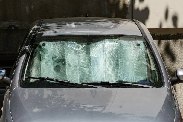 Foil sun shades under the windshield of a gray car parked outdoors on a sunny summer day. Reflective sun shield made of metallic silver foil protects vehicles from direct sunlight. stock photo