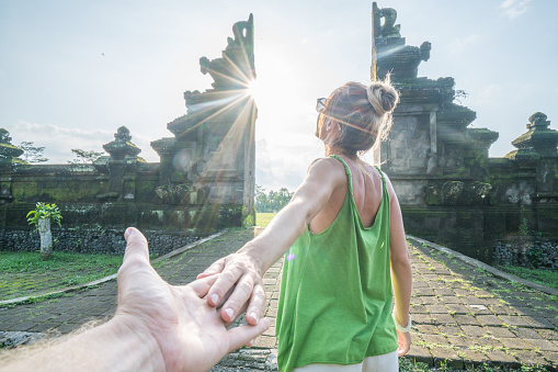 Follow me to concept, young woman leading boyfriend to Balinese gate at sunset, Indonesia 
 People travel positive emotion concept