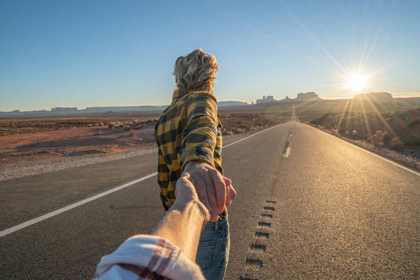 Follow me to concept; young man leading boyfriend to long highway road at sunset enjoying travel in the USA stock photo