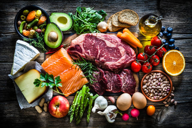 Food backgrounds: table filled with large variety of food Food backgrounds: top view of a rustic wooden table filled with different types of food. At the center of the frame is a cutting board with beef steak and a salmon fillet and all around it is a large variety of food like fruits, vegetables, cheese, bread, eggs, legumes, olive oil and nuts. Low key DSRL studio photo taken with Canon EOS 5D Mk II and Canon EF 70-200mm f/2.8L IS II USM Telephoto Zoom Lens meat stock pictures, royalty-free photos & images