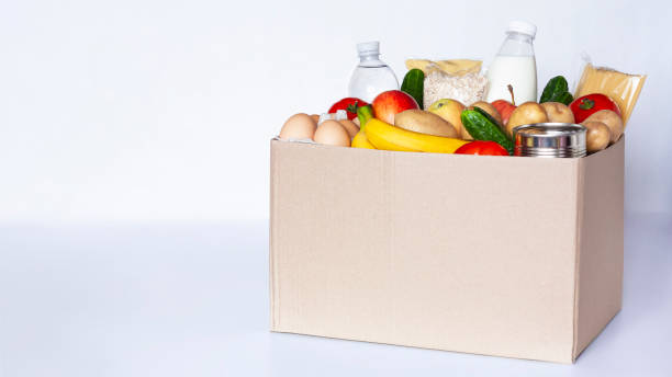 Food box on gray background Various grocery items in cardboard box on gray table. Food box with fresh vegetables, fruits, cereals, pasta, milk, eggs and canned goods. Food delivery or donation concept. Copy space. food donation stock pictures, royalty-free photos & images