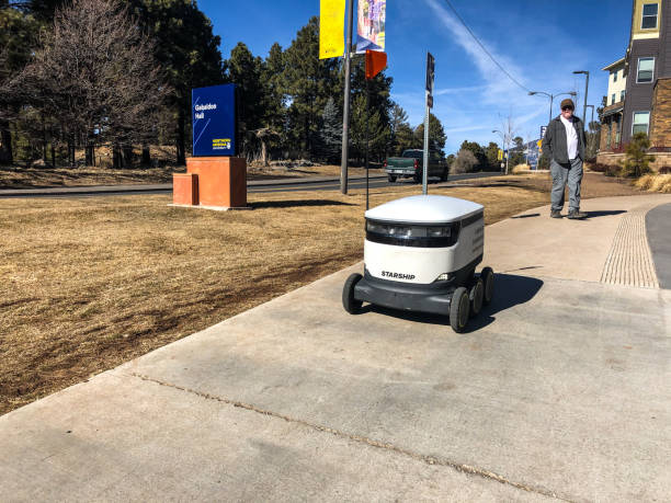 Food Delivery Robot on Campus Flagstaff, Arizona, USA - January 25, 2020: Northern Arizona University deploys a fleet of Starship autonomous robots that are used to deliver food to students in their dormitory, library or other locations on campus.  Students order and pay for the food on a smartphone app.  The product is loaded into the robot at a participating on-campus restaurant and then the robot is dispatched.  The robot finds the delivery location based on the GPS location of the student’s phone.  Order status is displayed on the student’s phone.  When the robot reaches the delivery location, in twenty minutes on average, the student is notified that the delivery has arrived.  The student then meets the robot and uses the app to unlock the robot and retrieve the food.  Northern Arizona University is in Flagstaff, Arizona, USA. jeff goulden people stock pictures, royalty-free photos & images