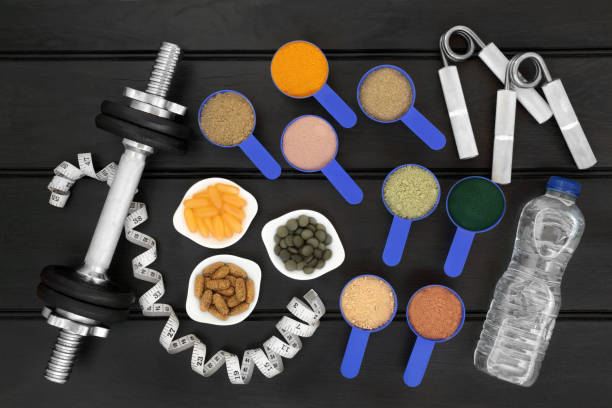 Food for Body Builders and Equipment Food for body builders with dietary supplement powders, water bottle, multi vitamins, fish oil and chlorella tablets with hand grippers, dumbbell weights and tape measure on wood background. pea protein powder stock pictures, royalty-free photos & images