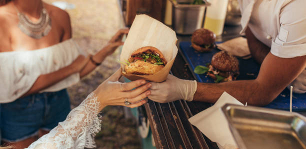 Food truck burger Woman hand reaching for a burger at food truck. Closeup of food truck salesman serving burger to female customer. food truck stock pictures, royalty-free photos & images