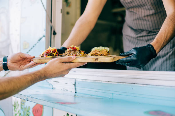 Food truck owner serving tacos to male customer. stock photo