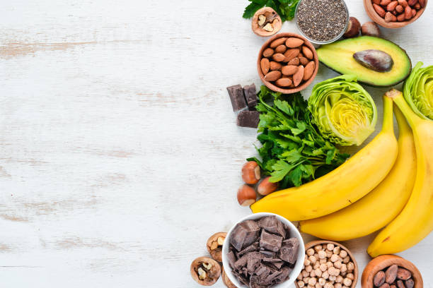 Foods containing natural magnesium. Mg: Chocolate, banana, cocoa, nuts, avocados, broccoli, almonds. Top view. On a white wooden background. Foods containing natural magnesium. Mg: Chocolate, banana, cocoa, nuts, avocados, broccoli, almonds. Top view. On a white wooden background. potassium stock pictures, royalty-free photos & images