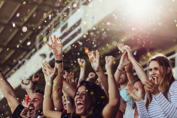 Football fans celebrating a victory in stadium Sports fans clapping hands in stands with falling confetti.  Football team supporters cheering in stadium. match sport photos stock pictures, royalty-free photos & images