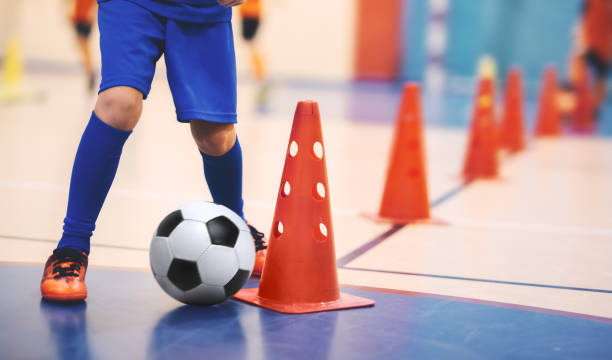 football futsal training for children. soccer training dribbling cone drill. indoor soccer young player with a soccer ball in a sports hall. player in blue uniform. sport background - futsal imagens e fotografias de stock