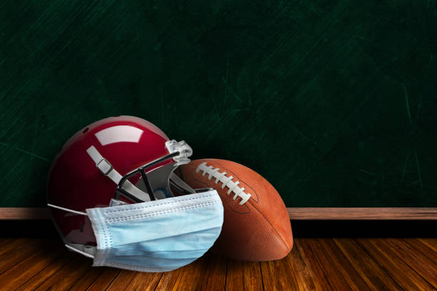 Football Helmet Wearing Mask With Chalkboard Background and Copy Space Football helmet wearing surgical mask on a background chalk board with copy space for text. Concept of COVID-19 coronavirus pandemic affecting American football season due to game or league suspensions or cancellations. american football sport stock pictures, royalty-free photos & images