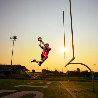 A football player catching the football in mid air at the goal post. Concept photo.