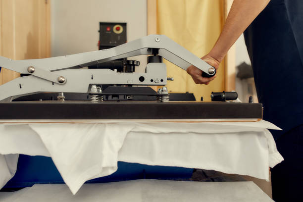 모든 인쇄 솔루션용. 티셔츠 인쇄를 위한 열 인쇄기 전송 기계를 사용하여 남성 노동자의 자른 샷 - 밀기 뉴스 사진 이미지
