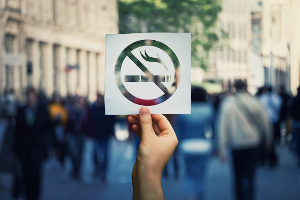 Forbidden area zone Hand holding a paper sheet with no smoking sign over a crowded street public place background. Forbidden area zone, restrictive symbol stop smoke. cigarette stock pictures, royalty-free photos & images