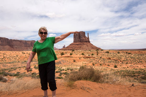 prospettiva forzata di una donna adulta anziana (anni '60) che finge di toccare una famosa formazione rocciosa nella utah monument valley - forced perspective foto e immagini stock