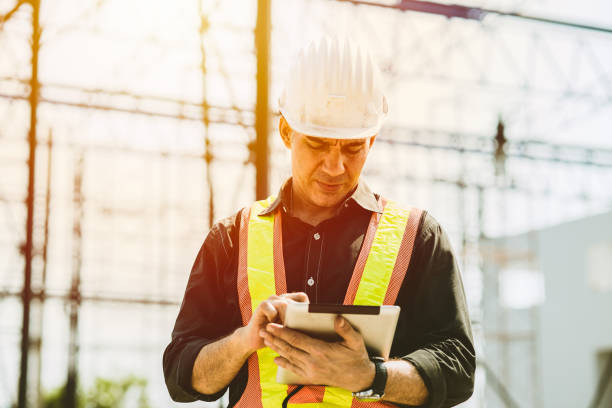 Foreman builder engineer worker using tablet computer to check building floor plan at construction site. stock photo
