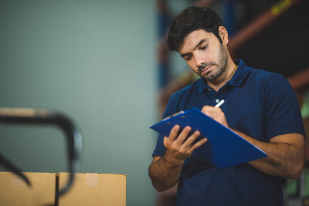 foreman project manager is working in store checking stock using tablet walkie talkie clipboard for work, warehouse storage, men in uniform blue t-shirt, working concept in storehouse. handsome portrait employee stock photo