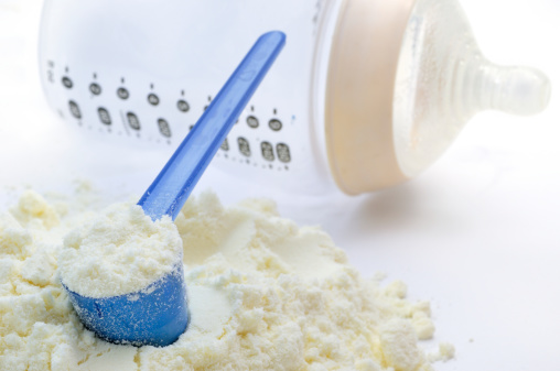 A close-up shot of baby milk formula with a plastic measuring spoon and bottle.