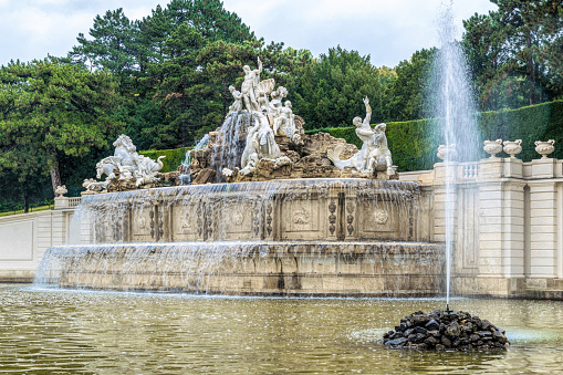 Vienna, Austria - October 07, 2021: luxurious blooming park and old baroque fountains in the park of Schonbrunn Palace near Vienna, Austria. Park ensemble in the garden of the ancient imperial palace and a strolling tourist