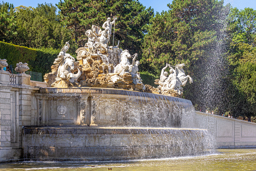 Vienna, Austria - August 12, 2022: luxurious blooming park and old baroque fountains in the park of Schonbrunn Palace near Vienna, Austria. Park ensemble in the garden of the ancient imperial palace and a strolling tourist