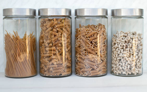 Four big glass jars with different whole grain pasta in the kitchen stock photo