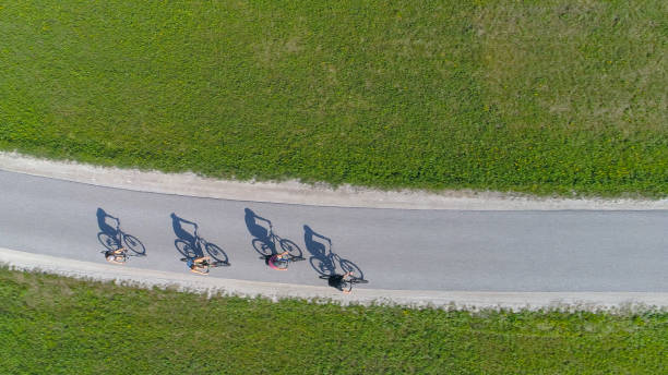 TOP DOWN: Four friends riding bikes casting shadows on the empty asphalt road. stock photo