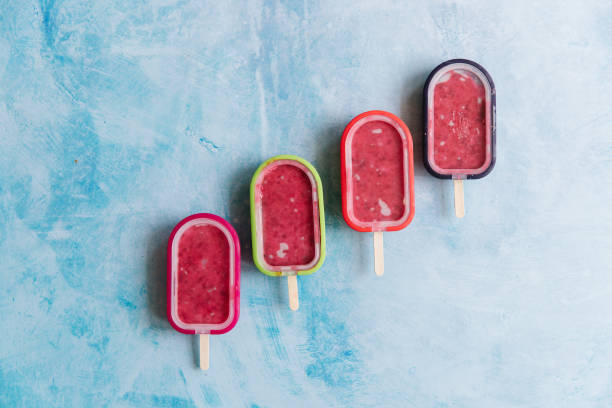 Four fruit popsicles with a wood popsicle stick on a blue background. stock photo
