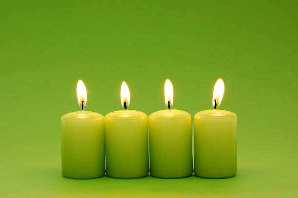 Four green candles in a row lit up stock photo