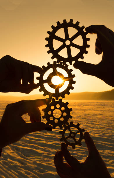 four hands are holding the gears against the sunset. stock photo