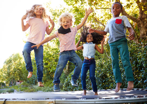 quattro bambini che si divertono insieme su un trampolino in giardino - trampolino foto e immagini stock