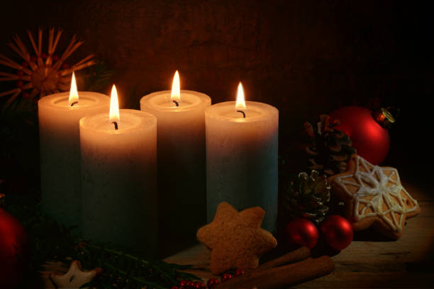 Four lighted candles for advent, Christmas decoration and gingerbread cookies against a dark brown rustic background, copy space, selected focus stock photo