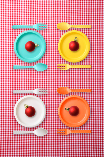Overhead shot of four pastel colored plastic place setting with red Christmas balls, on red gingham check tablecloth.