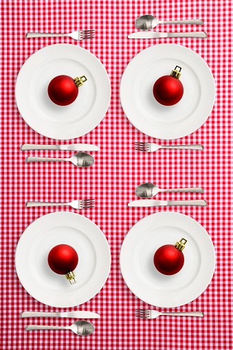 Overhead shot of four place setting with red Christmas ball on red gingham check tablecloth.