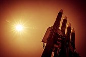Four rockets of anti-aircraft missile system are directed upwards against a background of bright sun. Orange toned image