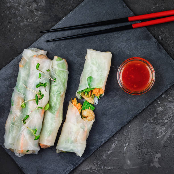 Four spring rolls lie on a black slate board, one of them is cut in half. A healthy Asian snack with vegetables in rice paper. stock photo