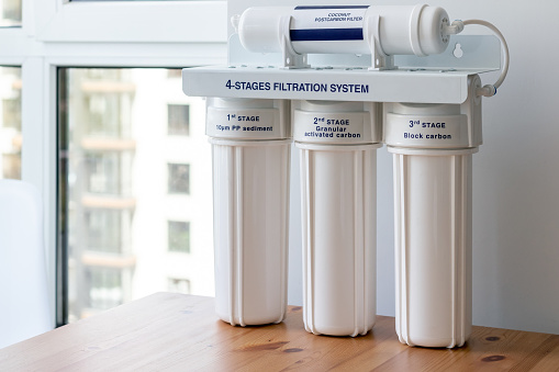 Four Stages Water Filtration System For The Home With Coconut Postcarbon Filter Granular Activated And Block Carbon On A Wooden Table Against A Blurred Window Background Reverse Osmosis System Stock Photo -