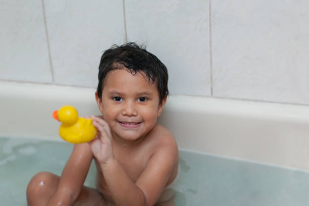 Four year old boy holding his favorite bubble bath toy while taking a bath. stock photo