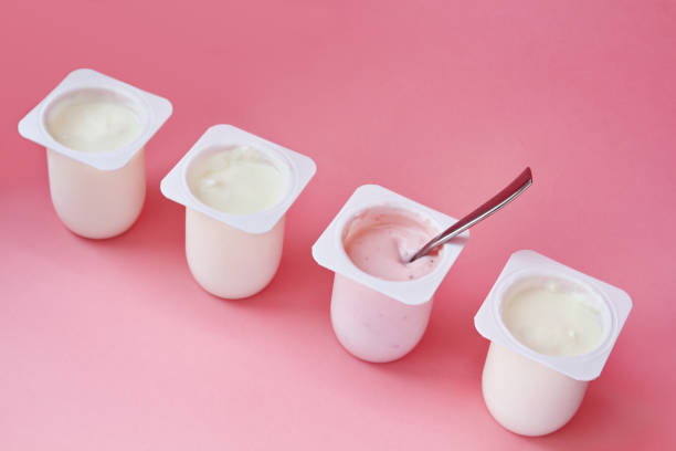 Four yogurts in white plastic cups on pink background in minimal style. stock photo