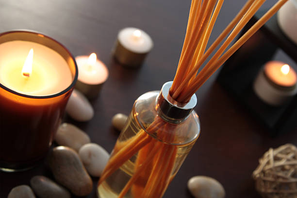 fragrance reed diffuser Close up of a bottle of fragrance diffuser with reeds. Tea light candles and an oil burner in the background. Shallow depth of field. aromatherapy stock pictures, royalty-free photos & images