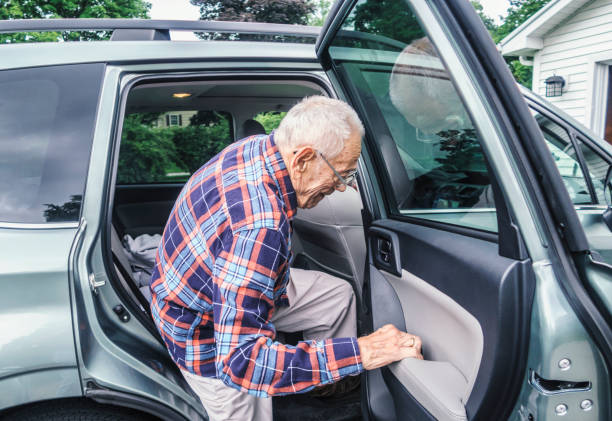 Frail Elderly Man Struggling to Exit From Car A physically impaired, real life, real person 95 year old senior adult man is struggling a bit - needing to concentrate on each individual move required by his frail arm and leg muscles to coordinate with each other to help him get out of the family car after a shopping trip. He's gripping the car door arm rest tightly as he deliberately exaggerates lifting each leg high enough to drag them both out of the car without stumbling or falling from the vehicle. His balance and stability have deteriorated significantly as he's gotten older. So he'll rely on his medical orthopedic equipment mobility walker - which is waiting just off camera - to grab for support when both feet finally hit the driveway.

Submitted to Getty/iStock image brief "Caregivers at Home" - Brief #775296211. open car door stock pictures, royalty-free photos & images
