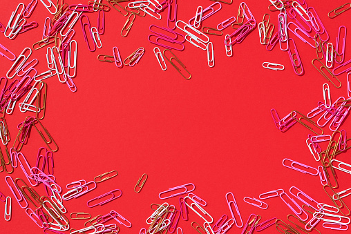 Frame of multicolored paper clips on red background. Back to school. Office, business, paperwork, education concept. Banner.