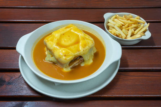 Francesinha is a Portuguese sandwich, made with bread, ham, linguica, sausage, steak, and covered with, cheese and beer sauce. Close up stock photo