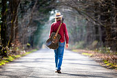 istock Free wandering man walking on country road with guitar on his back 1305946249