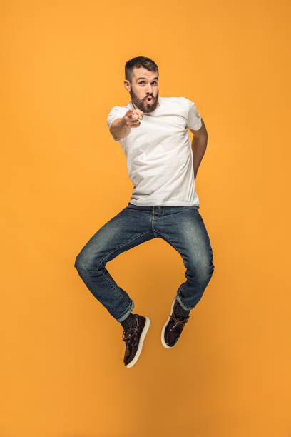 Freedom in moving. handsome young man jumping against orange background Freedom in moving. Mid-air shot of handsome happy young man jumping and gesturing against orange studio background. Runnin guy in motion or movement. Human emotions and facial expressions concept model object stock pictures, royalty-free photos & images